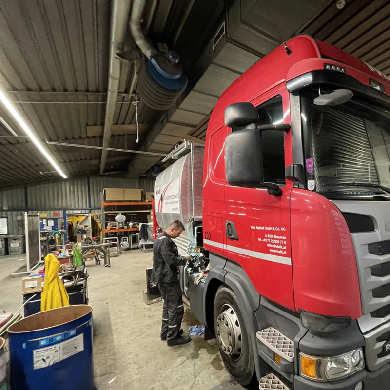 Ein roter Lkw wird in einer Werkstatt gewartet, mit einem Mechaniker, der an der Ausrüstung arbeitet. Hochwertige Instandhaltungsarbeiten.